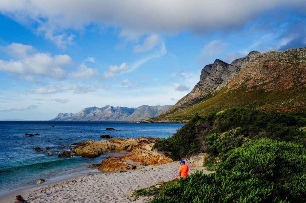 A man sitting on a rock by the shore with Kogelberg mountains in the background.