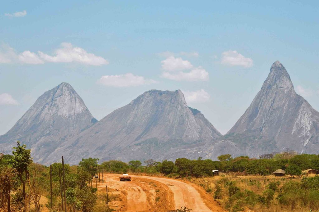 A road through the wilderness of Mozambique with the jagged peaks of towering mountains in the backdrop.