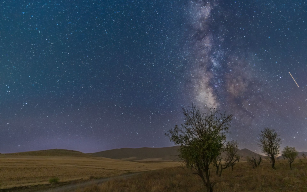 View of the Milky Way galaxy illuminating a vast, open grassland under the night sky in Sutherland, South Africa.