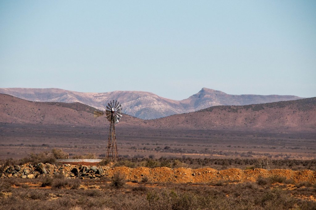 A windmill in the Karoo with the distant mountains under a blue sky.