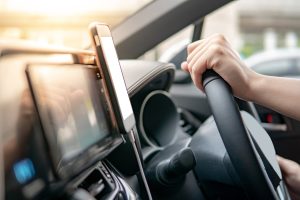 Male driver hand holding on steering wheel using smartphone for GPS navigation. Mobile phone mounting with magnet on the car console in modern car. Urban driving lifestyle with mobile app technology