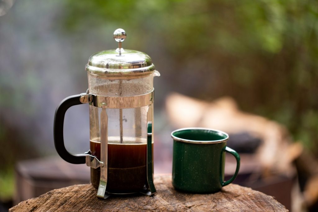 A coffee plunger and an enamel mug at a campsite.