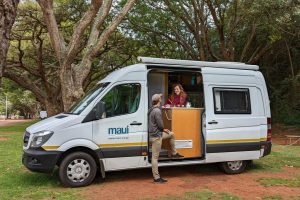 A couple stands inside and outside their RV rental vehicle.