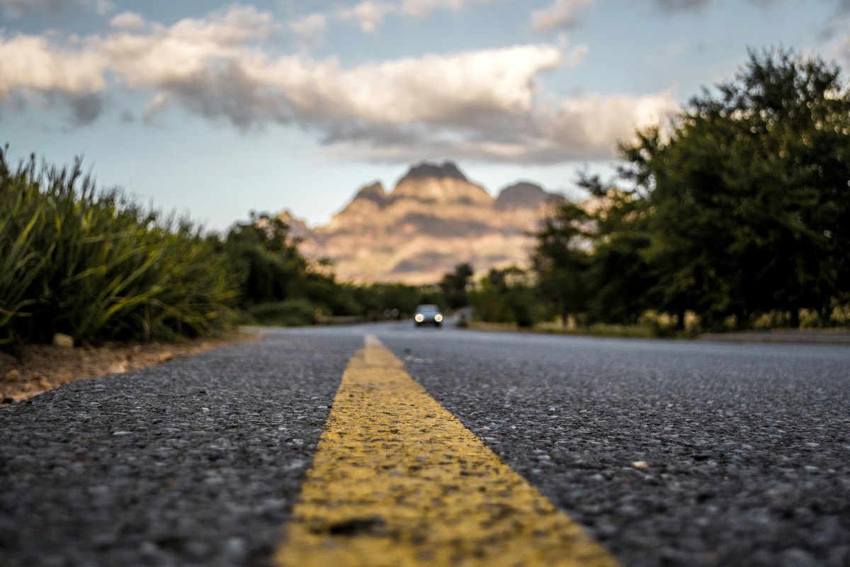 A car approaches on a tar road as part of a mountain road trip.