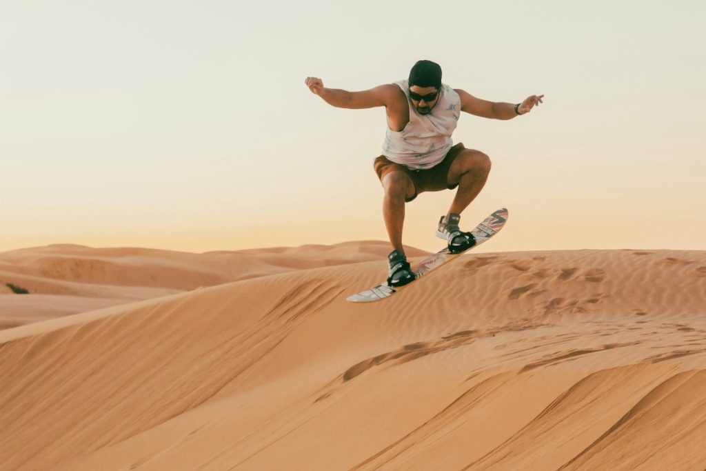 A man jumps on a sandboard in a desert.