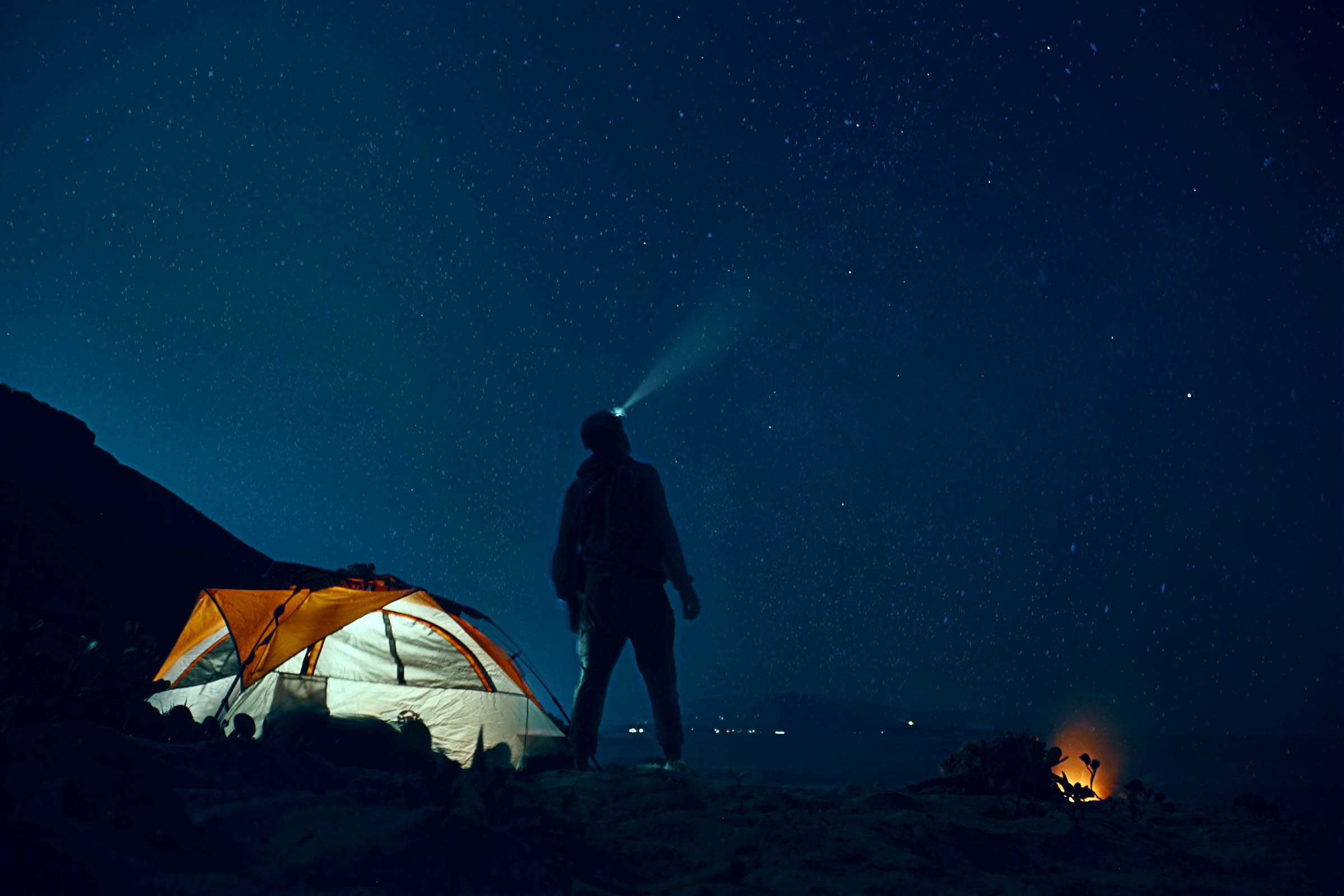 Een man wijst zijn hoofdlamp naar de sterren tijdens een kampeertrip | Foto: Unsplash