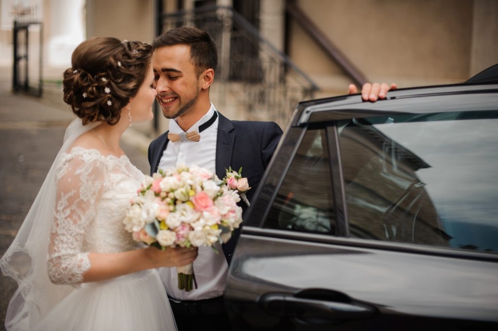 A bride and groom alongside their wedding car.