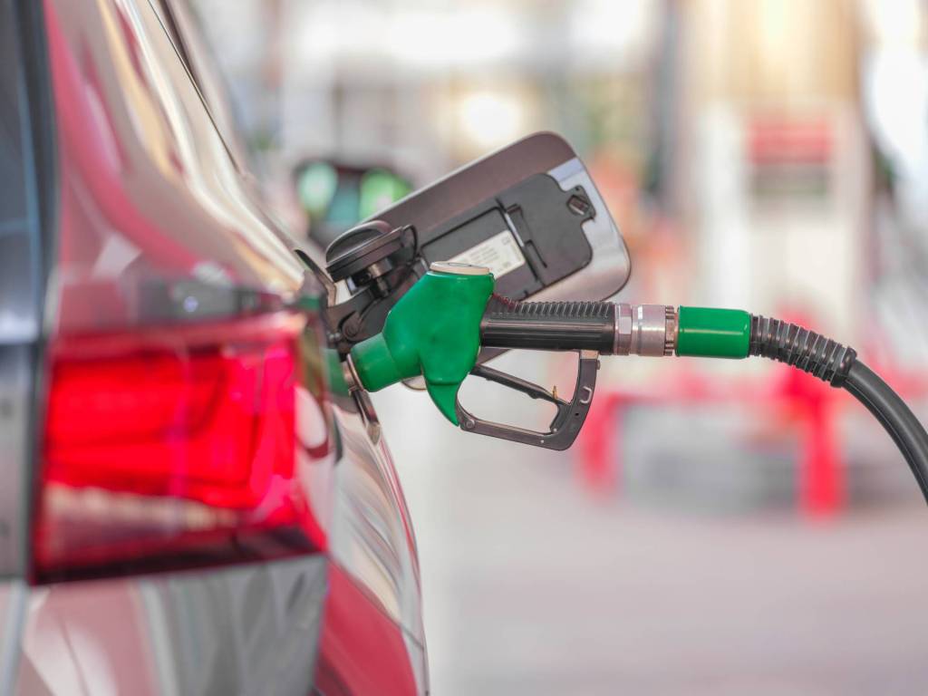 A car at a fuel station with a pump in the fuel inlet.
