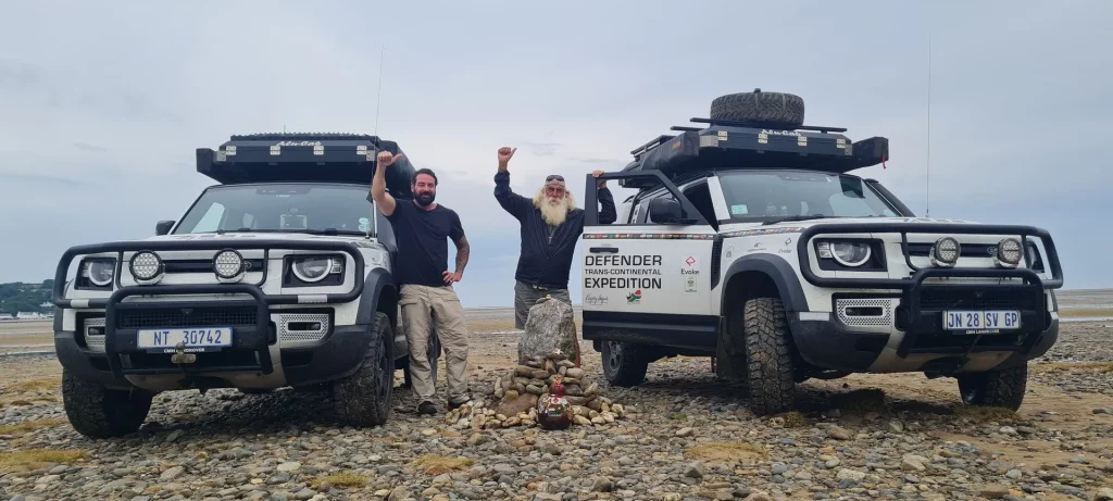 Kingsley Holgate standing beside two Land Rovers