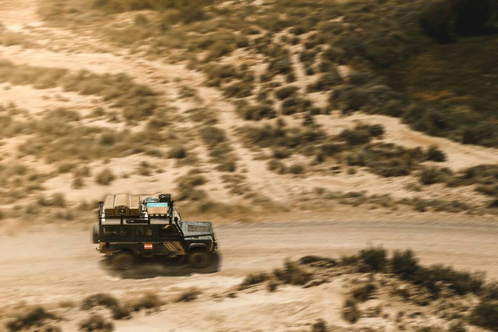 4x4 safari vehicle driving along sandy dirt road through dry bushland