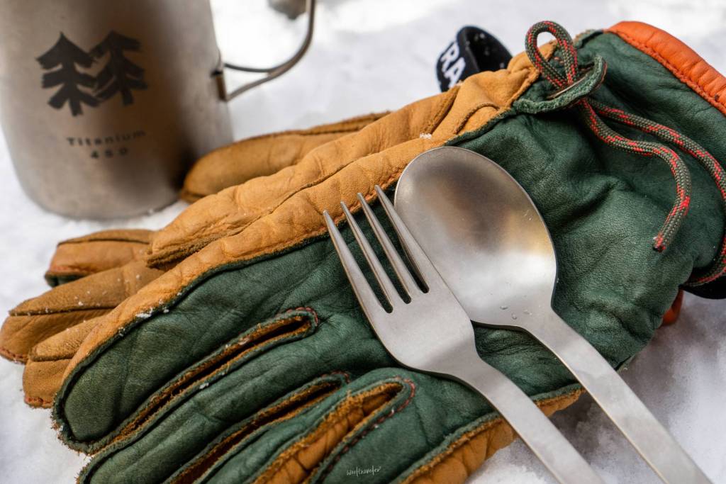 Gloves, a spoon, fork and a mug on the snow.