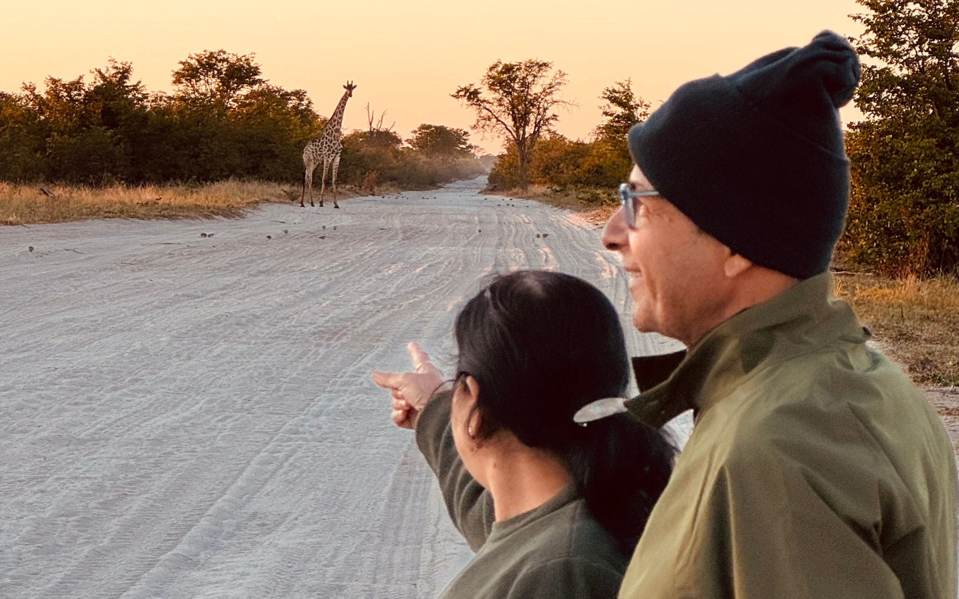 Tourists watching in awe as a giraffe crosses a tar road in the distance during a self-drive adventure in Botswana.