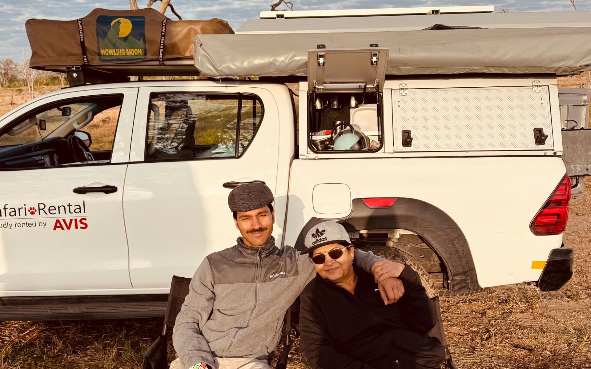 A mother and son seated on camper chairs in front of a 4x4 rental vehicle during a self-drive adventure in Botswana.