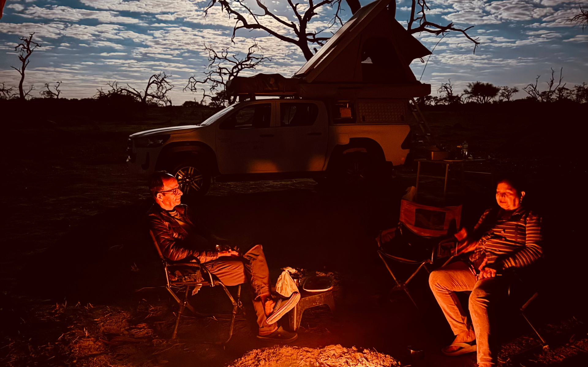 Tourists relaxing by the bush fire at dusk during a self-drive adventure in Botswana.